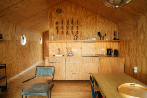 Interior of a Wikkel tiny house at De Klepperstee, Netherlands, featuring plywood walls and a compact kitchen.