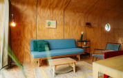 Modern living room in the Wikkel tiny house at De Klepperstee, featuring wood walls, blue sofa, and warm light.