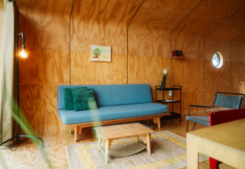 Moderne woonkamer in het Wikkel tiny house op De Klepperstee, houten wanden, blauwe bank en sfeerverlichting.