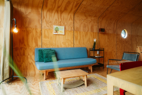 Modern living room in the Wikkel tiny house at De Klepperstee, featuring wood walls, blue sofa, and warm light.