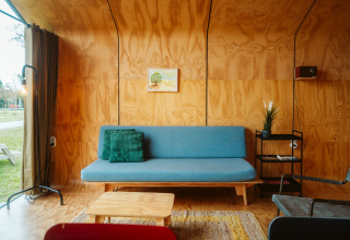 Moderne stue i Wikkel tiny house med blå sofa, grøn pude og trægulve i Holiday park De Klepperstee, Holland.