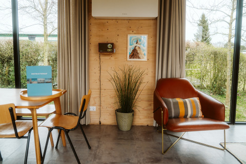 Interior de una moderna cabaña en Kleproos, De Klepperstee, Países Bajos, con sillón, mesa y ventanales.