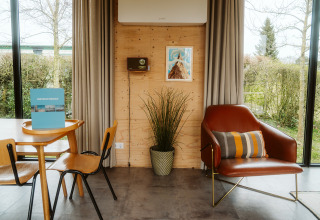 Interior de una moderna cabaña en Kleproos, De Klepperstee, Países Bajos, con sillón, mesa y ventanales.