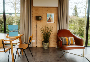 Modernes Lodge-Interieur in Kleproos, De Klepperstee, Niederlande; Sessel, Tisch und große Fenster.