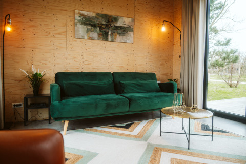 Gezellige zithoek in lodge Kleproos, De Klepperstee, met groene zetel en groot raam op het park.