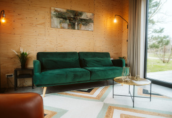 Hyggelig lodge-stue på Kleproos ved De Klepperstee, med grøn sofa, moderne bord og store vinduer.