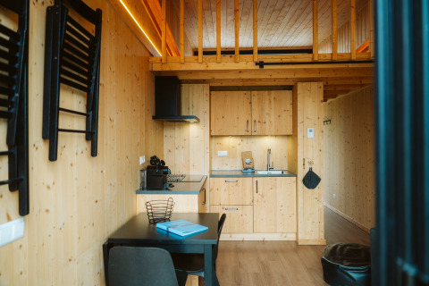 Modern tiny house with wooden kitchen, dining table, and mezzanine at De Klepperstee Holiday Park, Netherlands.