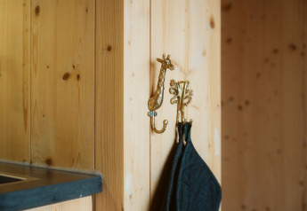 Twee gouden dierenhaakjes aan een houten wand in het tiny house Klaproos, De Klepperstee, Nederland.