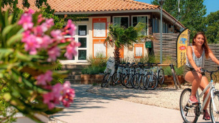 Woman riding a bike past the reception at Camping Seasonova Ensoya holiday park in Occitanie, France.