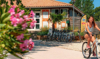 Woman riding a bike past the reception at Camping Seasonova Ensoya holiday park in Occitanie, France.