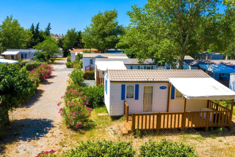 Foto van een gezellige chalet met houten terras, omringd door bomen en bloeiende struiken in de zomer.
