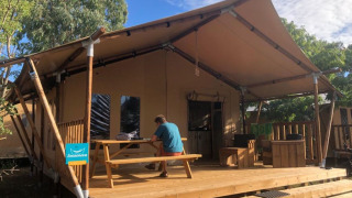 Une personne est assise à une table de pique-nique devant une tente safari appelée Wood lodge par une journée ensoleillée.