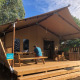 A person sits at a picnic table in front of a safari tent named Wood lodge on a sunny day.