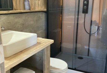 Baño en la tienda safari Wood lodge en Camping Seasonova Ensoya, Francia, con ducha moderna y madera.
