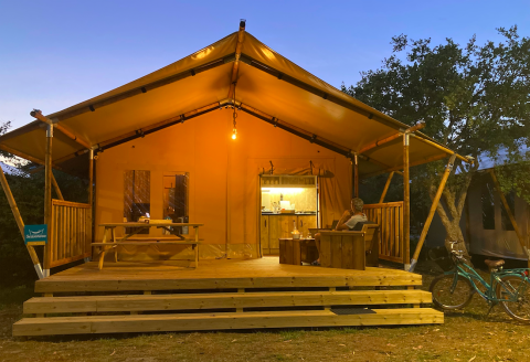 Tente safari Wood lodge au Camping Seasonova Ensoya en France, vue extérieure au crépuscule avec terrasse éclairée.