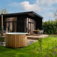 Lodge moderno chiamato Wellness Boutique con vasca esterna, terrazza in legno e giardino verde rigoglioso.