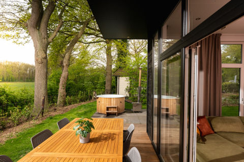 Wellness Boutique Lodge im Holiday Park Mölke, Terrasse mit Esstisch und Whirlpool im grünen Garten.