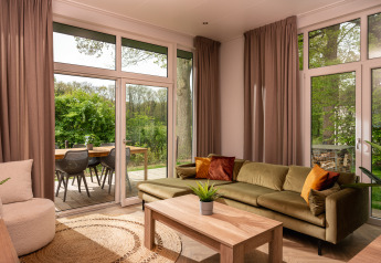 Woonkamer in Wellness Boutique, Holiday Park Mölke, met groene zetel, houten tafel en tuinzicht.
