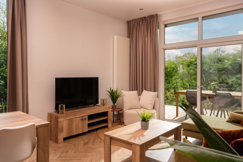 Helles Wohnzimmer in der Wellness Boutique im Holiday Park Mölke mit Blick auf die grüne Terrasse draußen.
