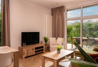 Sala luminosa y acogedora en Wellness Boutique de Holiday Park Mölke con TV y vista a la terraza exterior.