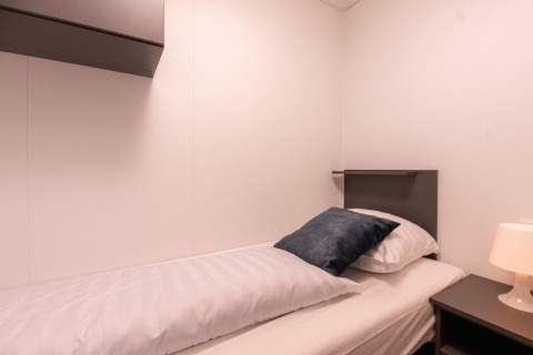 En moderne enkeltværelsessuite med enkelt seng, natbord og bordlampe i Wellness Boutique på Holiday Park Mölke.