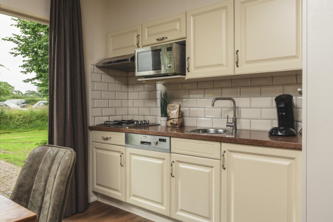 Moderne kitchenette met crèmekleurige kasten, gasvuur, spoelbak en koffiemachine in een vakantielodge.