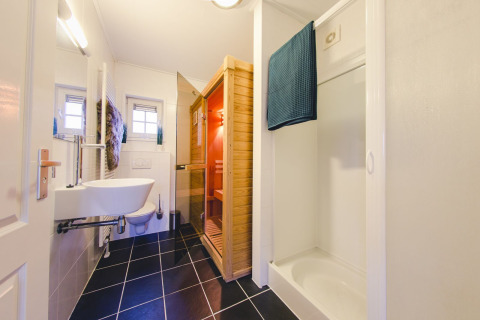 Moderne badkamer met zwart tegelvloer, sauna, douche en toilet in groepsaccommodatie in Nederland.