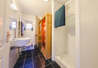 Salle de bain moderne avec sol en carrelage noir, sauna, douche et WC dans un hébergement de groupe aux Pays-Bas.
