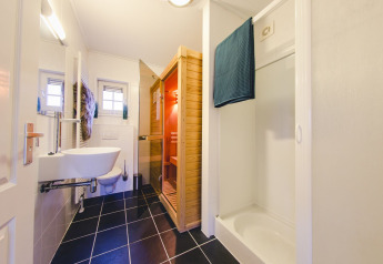 Moderne badkamer met zwart tegelvloer, sauna, douche en toilet in groepsaccommodatie in Nederland.