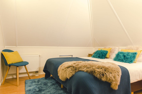 Gezellige slaapkamer in lodge met tweepersoonsbed, blauwe en gele kussens bij Holiday Park Mölke.