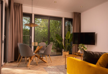 Salón moderno de lodge con grandes ventanales, mesa de cristal, sillas grises y sofá amarillo, vista verde.