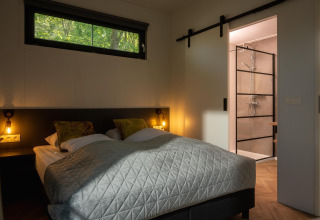 Dormitorio en Happy Oak Lodge de Holiday Park Mölke, con cama doble, ventana y baño con ducha moderna.