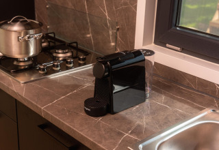 Moderne keuken met espressomachine, gasfornuis, kookpot en raam in Happy Oak Lodge, Holiday Park Mölke.