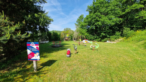 Area giochi al Camping La Perle in Nouvelle-Aquitaine, Francia, circondata dal verde e cielo sereno.