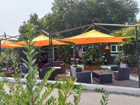Sitzbereich im Freien mit gelb-orangenen Sonnenschirmen im Camping La Perle, Nouvelle-Aquitaine, Frankreich.