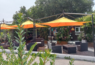 Sitzbereich im Freien mit gelb-orangenen Sonnenschirmen im Camping La Perle, Nouvelle-Aquitaine, Frankreich.