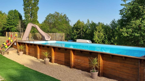 Outdoor swimming pool with slide and wooden paneling, surrounded by plants at Camping La Perle, Nouvelle-Aquitaine.