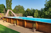 Piscina all'aperto con scivolo e pannelli in legno, circondata da piante al Camping La Perle, Nouvelle-Aquitaine.