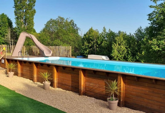 Udendørs swimmingpool med rutsjebane og træpaneler, omgivet af planter i Camping La Perle, Nouvelle-Aquitaine.