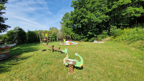 Spielplatz im Camping La Perle, Nouvelle-Aquitaine, Frankreich, mit Schaukeln, Wippe und Wiese.