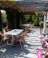 Udendørs siddeområde på Camping La Perle i Nouvelle-Aquitaine, Frankrig, med borde, stole og blomster.