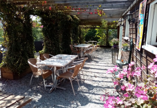 Udendørs siddeområde på Camping La Perle i Nouvelle-Aquitaine, Frankrig, med borde, stole og blomster.