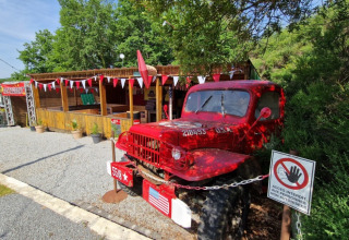 Camion vintage rouge au Camping La Perle en Nouvelle-Aquitaine, France, près d’un chalet en bois.
