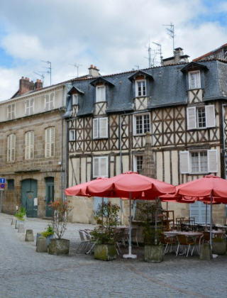 Charmerende brostensbelagt gade med gamle bindingsværkshuse og café med røde parasoller i Saint-Médard-la-Rochette.