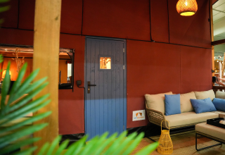 Indendørsfoto af Wander Lodge på Holiday park De Boshoek i Holland med sofa, blå dør og hyggelig belysning.
