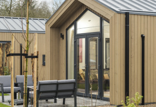 Modern tiny lodge with hot tub, large windows, and patio at Veluwepark de Bosgraaf, Netherlands.