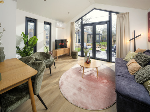 Sala moderna en Tiny Lodge con grandes ventanales y vista al jardín en Veluwepark de Bosgraaf, Países Bajos.