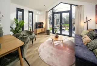 Sala moderna en Tiny Lodge con grandes ventanales y vista al jardín en Veluwepark de Bosgraaf, Países Bajos.