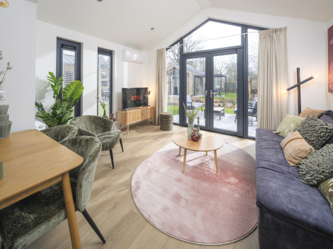 Modern living room in Tiny Lodge with large windows and garden view at Veluwepark de Bosgraaf, Netherlands.