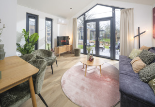 Soggiorno moderno in Tiny Lodge con grandi finestre e vista giardino al Veluwepark de Bosgraaf, Paesi Bassi.